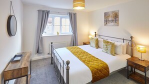 A neatly arranged bedroom with a bed, bedside tables, a window with curtains, a radiator, and a painting on the wall. - Host Stay Redsky House (Whitby)