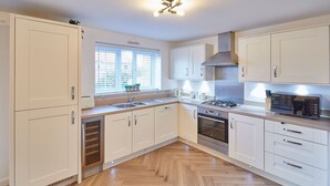 A modern kitchen with white cabinets, a built-in oven, a microwave, and a window with blinds. - Host Stay Redsky House (Whitby)