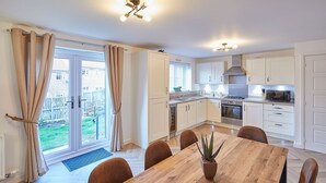 A modern kitchen with white cabinets, a dining table with chairs, and a view of the backyard through the glass door. - Host Stay Redsky House (Whitby)