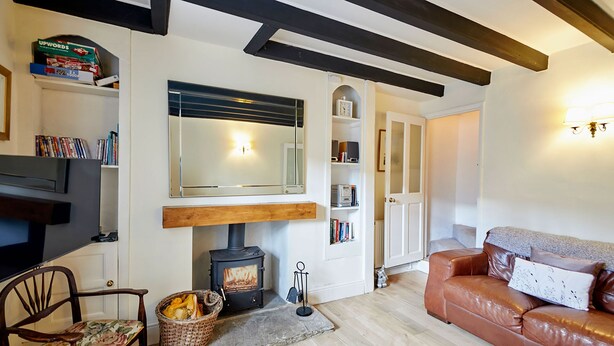 Ein gemütliches Wohnzimmer mit Kamin, Holzbalken, einem Ledersofa und einem Bücherregal.