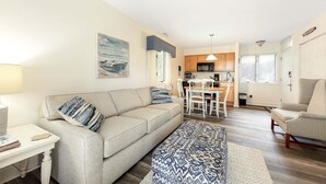 Ein Wohnzimmer mit einer Couch, einem Esstisch und einer Küche im Hintergrund.