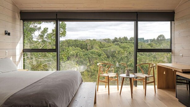 A bedroom with a large window, a bed, and a desk with two chairs.