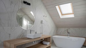 A modern bathroom with a freestanding bathtub, a wooden vanity with a sink, a large mirror, and a skylight.