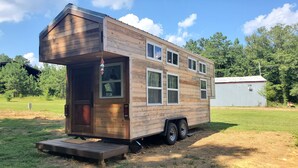 A mobile home with a front porch, multiple windows, and a small attached shed. - Pleasant Grove Tiny Home! (Pell City)
