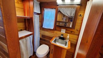 A compact wooden bathroom with a toilet, sink, and a mirror above it.