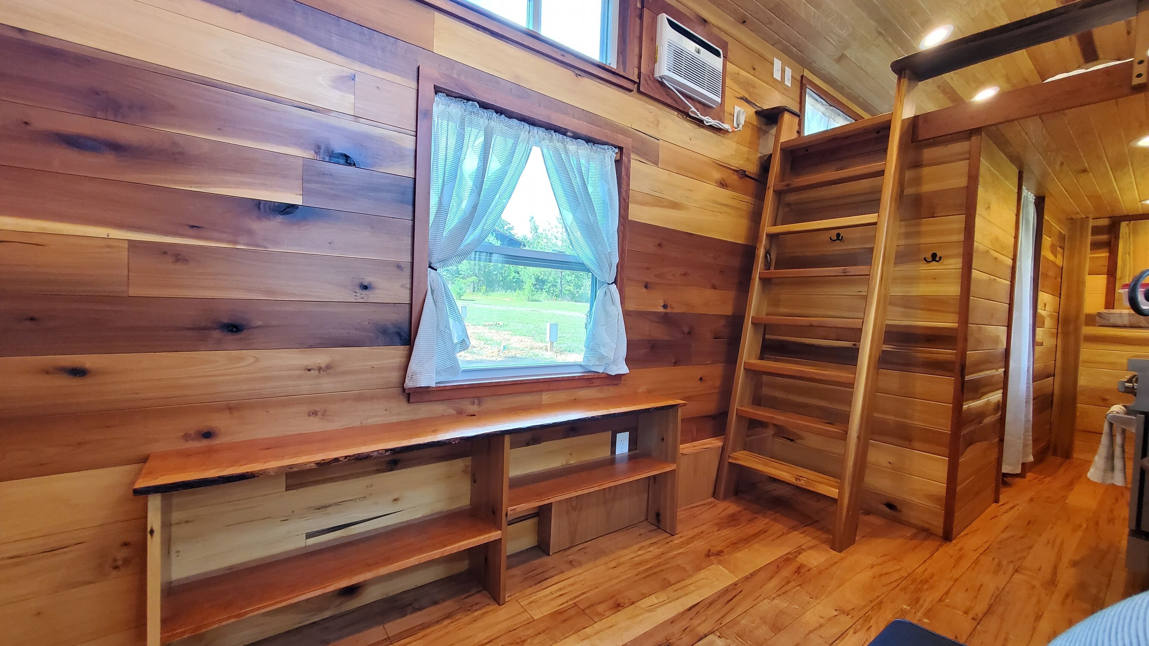 A wooden interior with a window, built-in shelves, and a ladder.