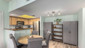 A compact kitchen with wooden cabinets, a microwave, and a refrigerator. There is a dining table with four chairs and a ceiling light fixture above it. - 1 Bedroom Condo, Sparkling Pool, Fitness Center, Pets Welcome (Glendale)
