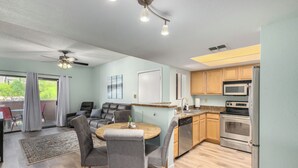 A modern kitchen with a dining area, featuring a round wooden table, grey upholstered chairs, and a ceiling fan. - 1 Bedroom Condo, Sparkling Pool, Fitness Center, Pets Welcome (Glendale)