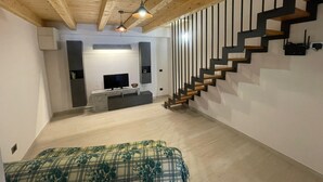 A modern interior with a wooden ceiling, a staircase with black railings, a flat-screen TV on a white console, and a patterned bedspread. - La Dimora nelle Rue (Civitella Roveto)