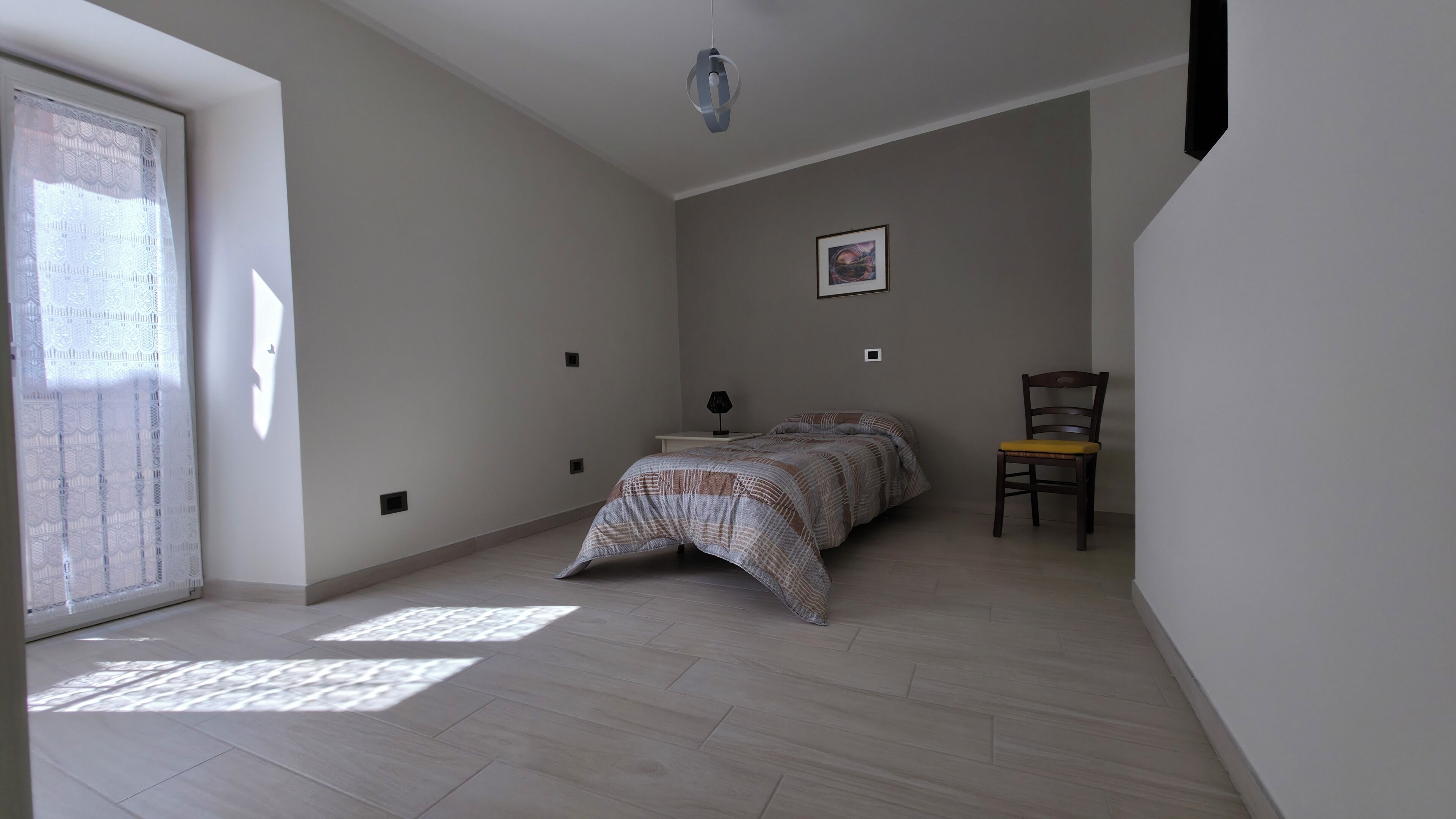 Un dormitori amb un llit, una cadira, una taula de nit, una làmpada i un quadre a la paret.