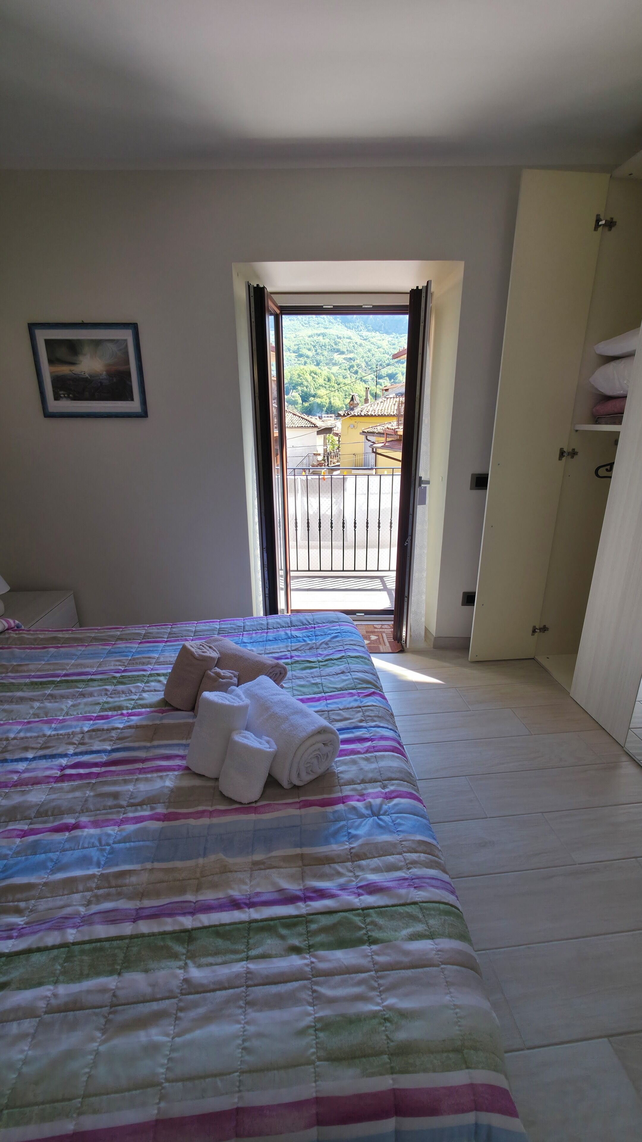 A bedroom with a bed, a door leading to a balcony, and a framed picture on the wall.