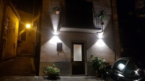 A narrow street with a building featuring a door, a small balcony with plants, and a parked car. - La Dimora nelle Rue (Civitella Roveto)