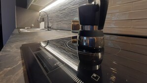 A kitchen with a black induction cooktop, a stainless steel coffee maker, and a modern faucet. - La Dimora nelle Rue (Civitella Roveto)