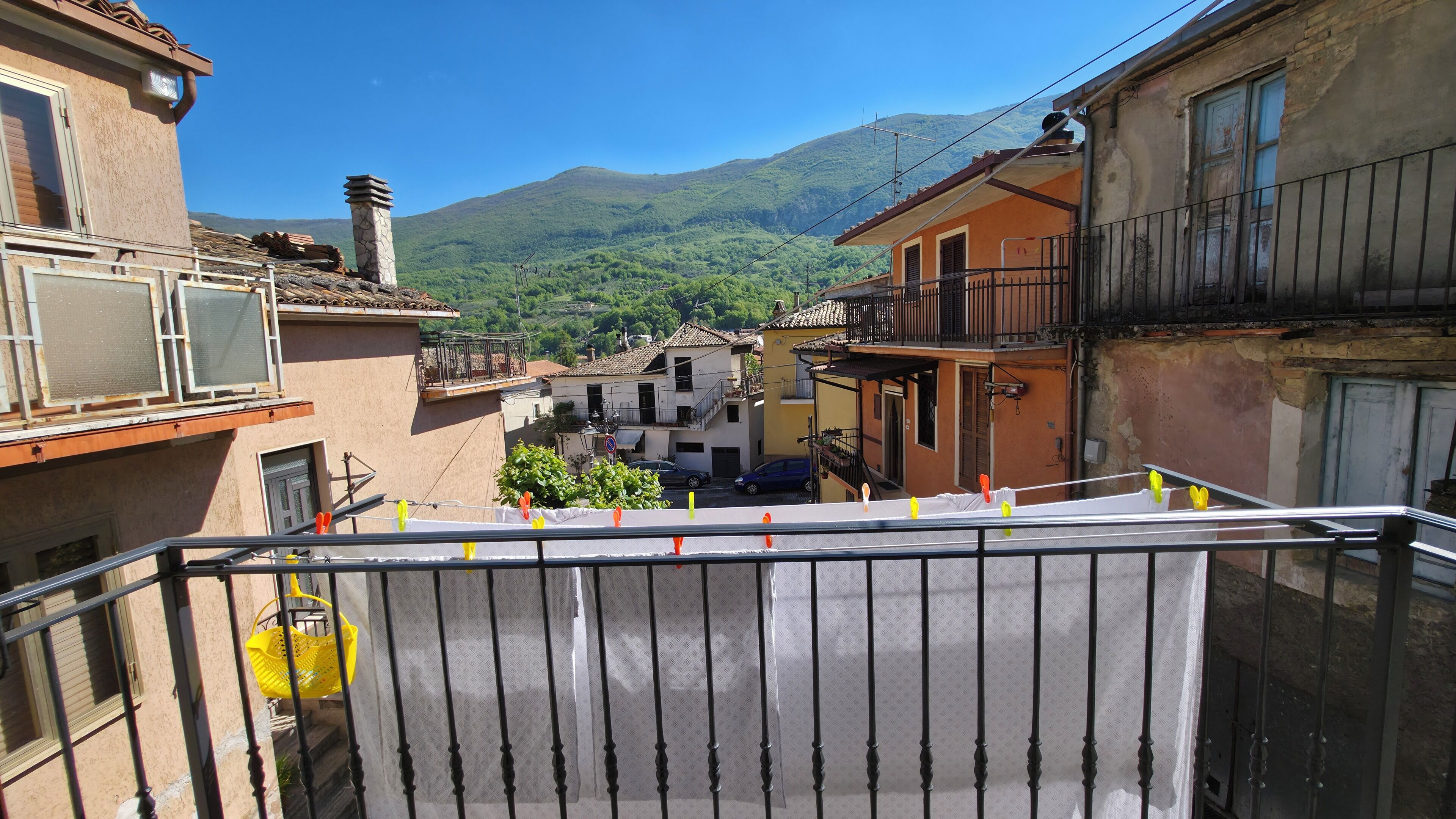 A narrow street with buildings, a balcony, and a mountain in the background.
