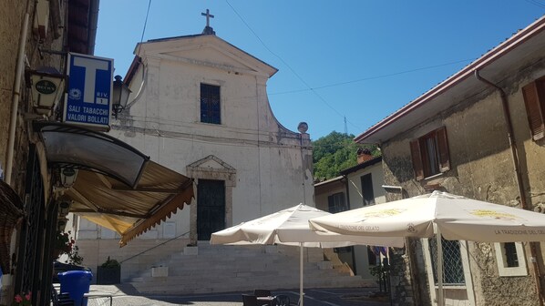 Una iglesia con un campanario, un letrero de 'Beck's Salt Tobacco Valori Bollati' y sombrillas exteriores con la marca 'La Tradizione del Gelato'.