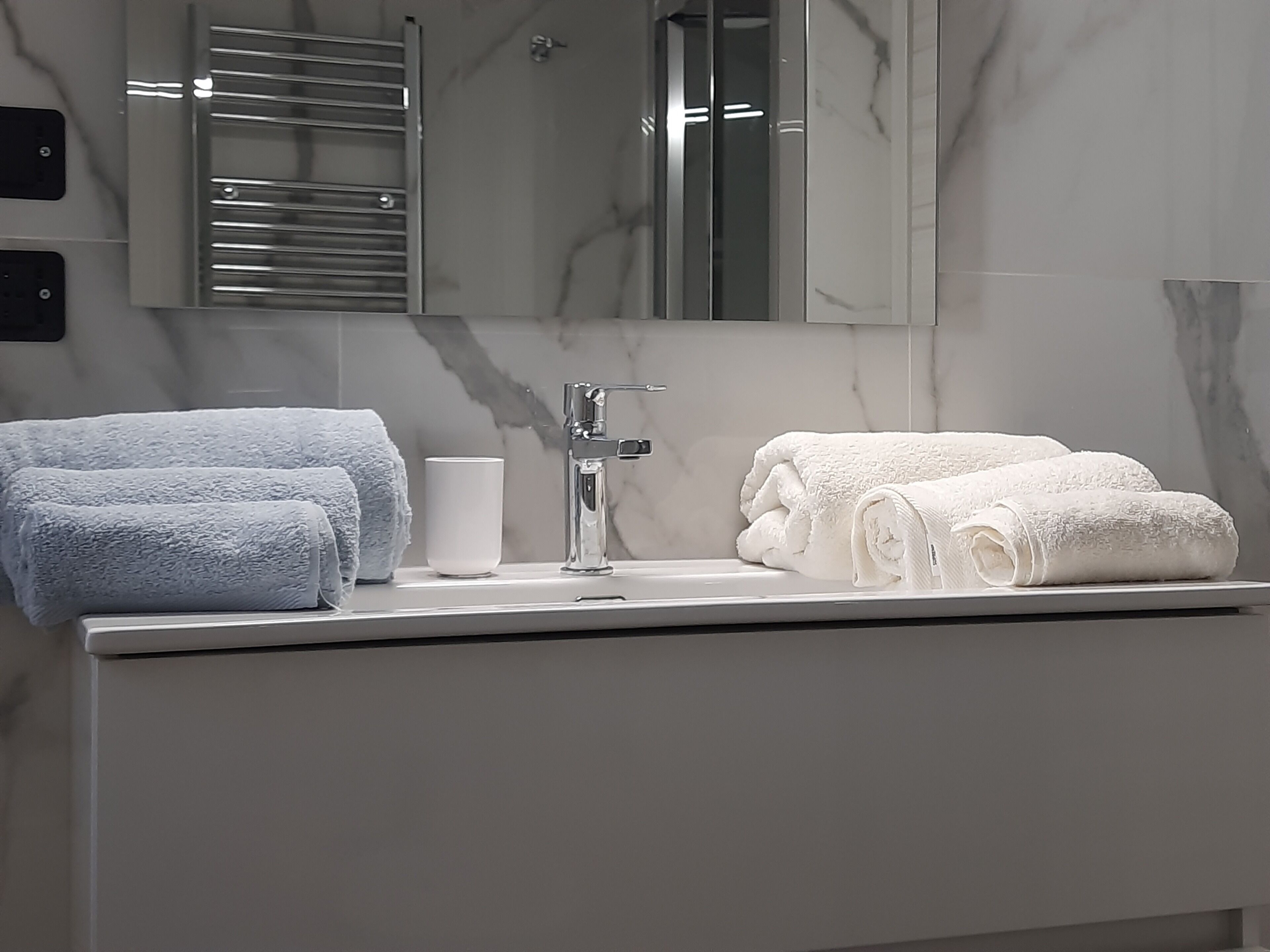 Un baño con lavamanos de mármol, dos toallas (una azul y una blanca) y una taza.