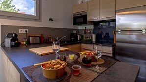 A modern kitchen with wooden cabinets, a stainless steel refrigerator, and a large window. - Le Coquelicot (Annecy)
