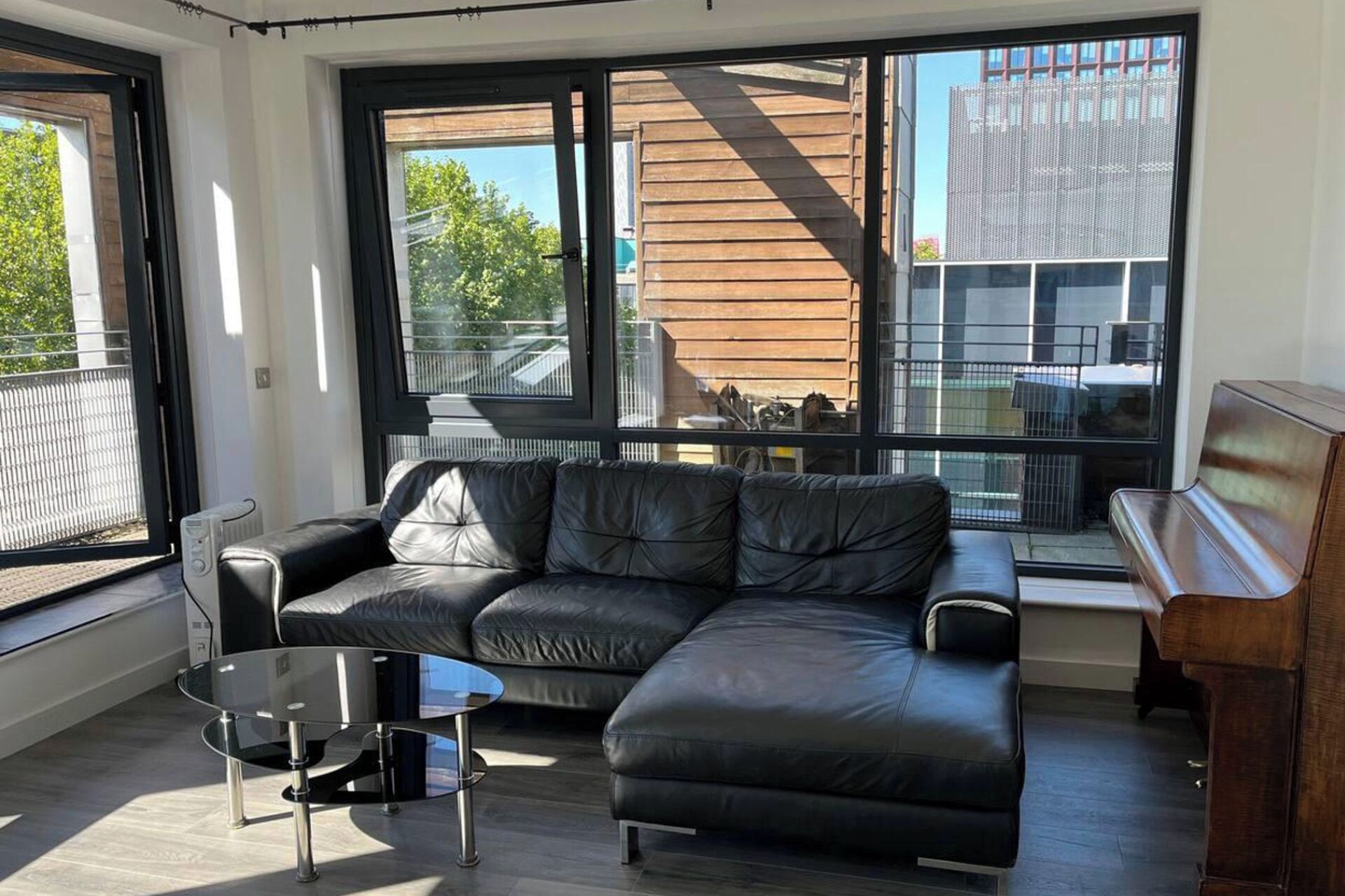 Ein modernes Wohnzimmer mit einem Ledersofa, einem Glastisch und einem Klavier.