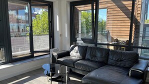 Ett modernt vardagsrum med en svart lädersoffa, ett soffbord i glas och stora fönster med utsikt över staden.
