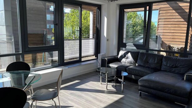 Ett modernt vardagsrum med en svart lädersoffa, ett soffbord i glas och en matplats med ett bord och stolar i glas. Stora fönster ger utsikt över omgivningen.