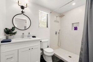 A modern bathroom with a white vanity, a toilet, a shower, and a small shelf with toiletries.