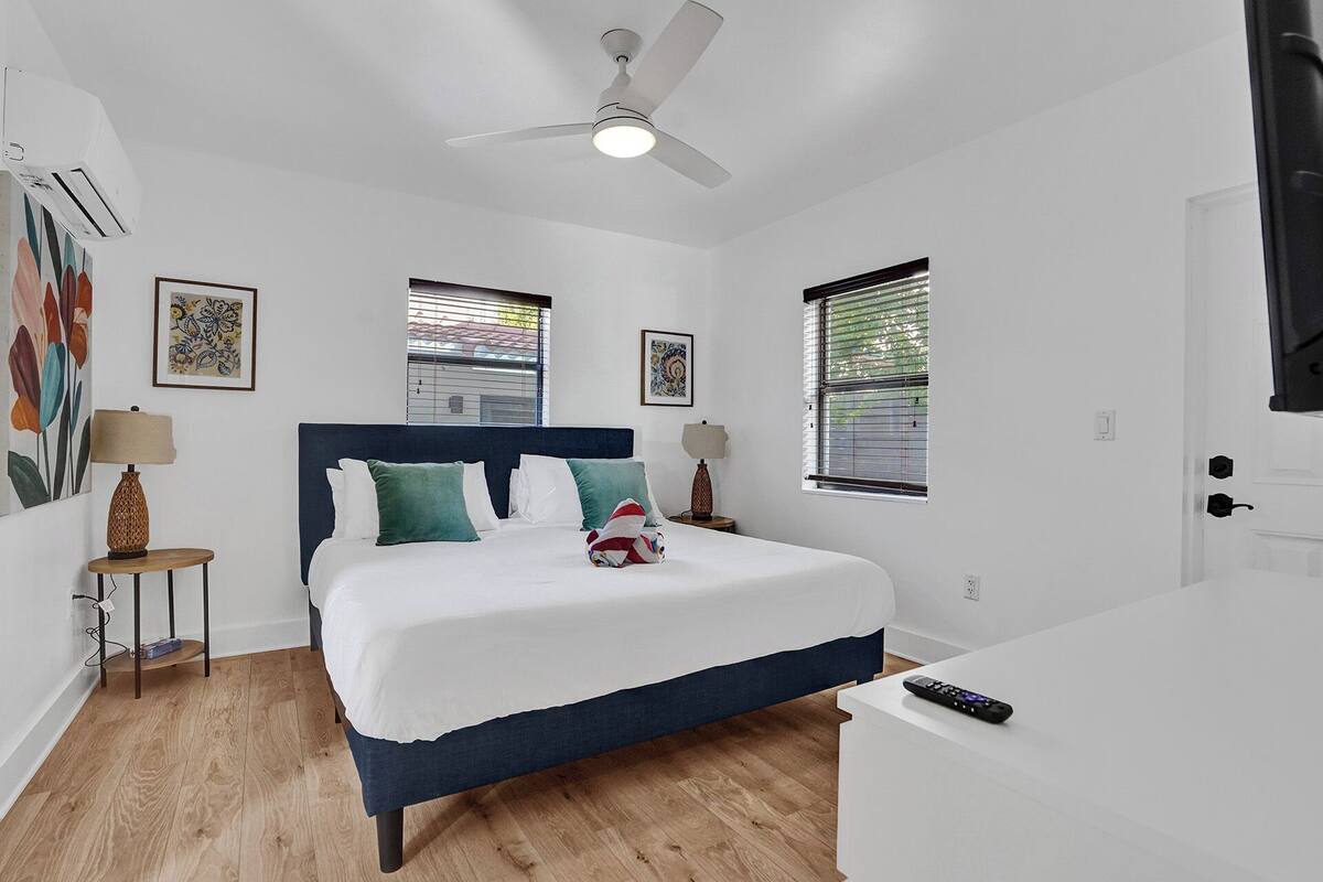 Un dormitorio con cama, ventilador de techo, dos mesitas de noche con lámparas y una puerta.