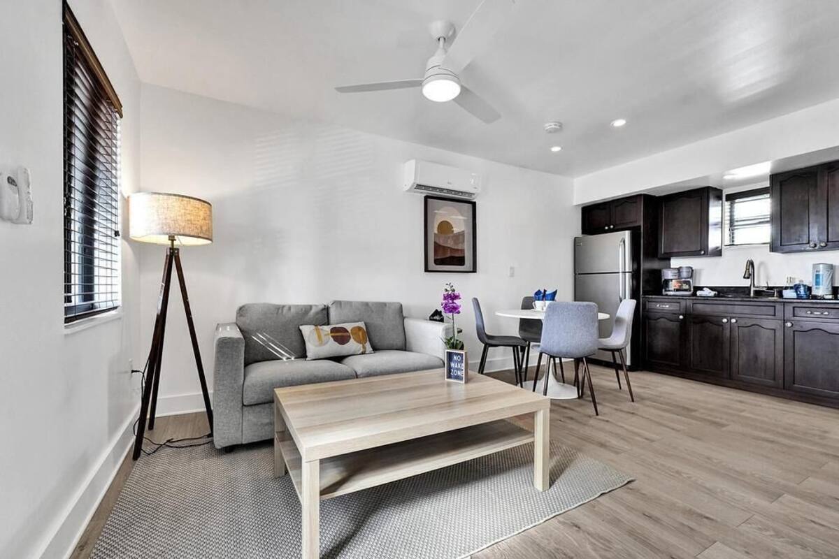 Una sala moderna con un sofá gris, una mesa de centro de madera y un comedor con una mesa y sillas blancas.