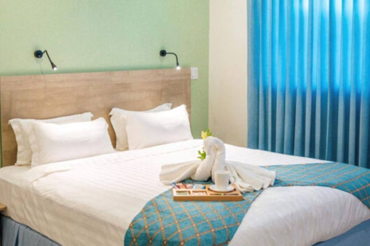 Una cama bien hecha con sábanas blancas, una manta estampada en azul y una toalla doblada en forma de cisne.