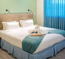 Uma cama bem arrumada com lençóis brancos, um cobertor estampado em azul e um arranjo de toalhas em forma de cisne.