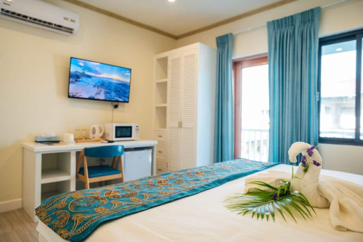 Habitación de hotel con una cama, un escritorio con silla, televisor y ventana con cortinas.