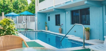 Una piscina con escalera de metal, rodeada de sillas de descanso y sombrillas.
