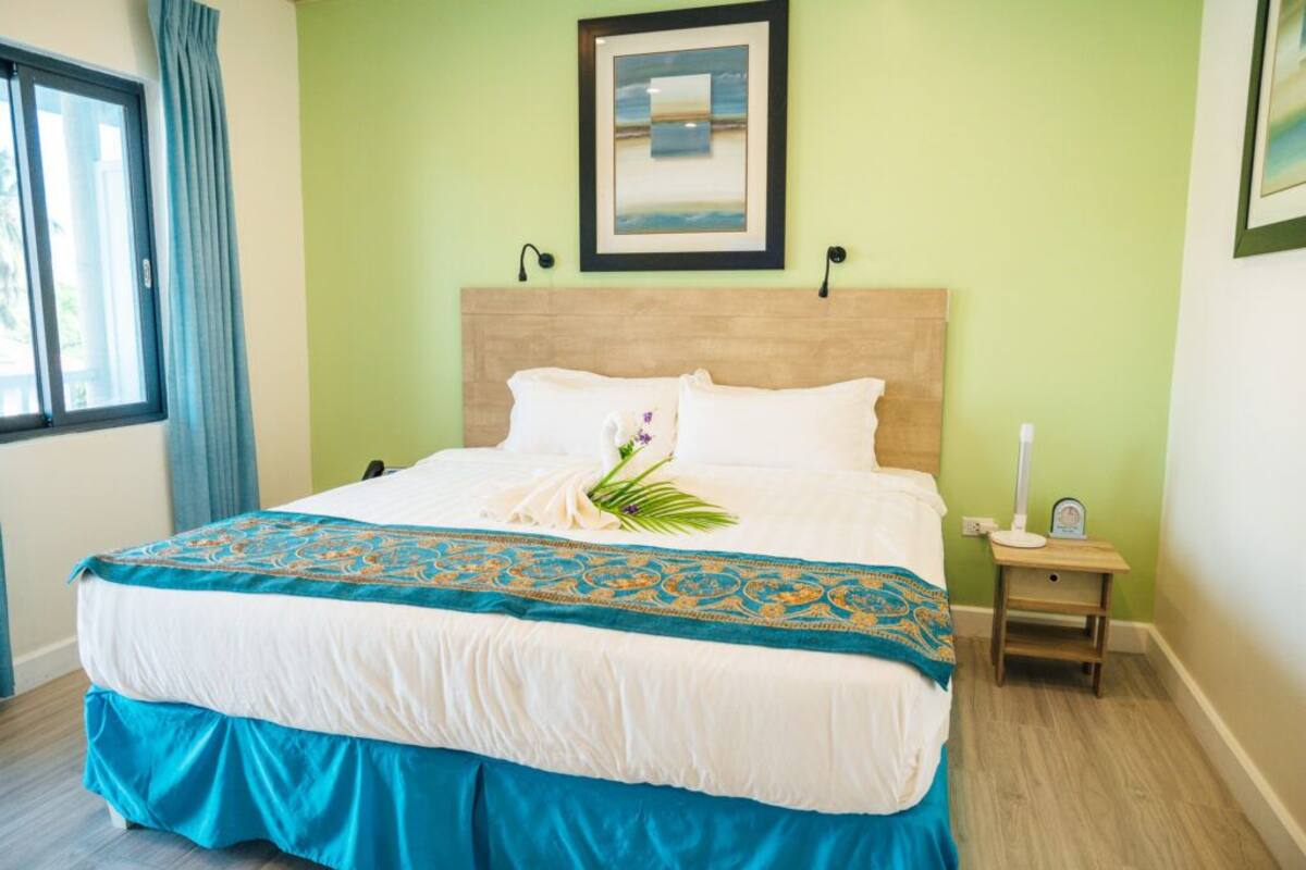 Habitación de hotel con cama, mesita de noche, un cuadro en la pared y una ventana con cortinas.