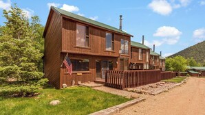 A two-story wooden building with a green roof, a flag, and a fenced driveway.