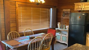 A wooden interior with a dining table, chairs, a refrigerator, and a kitchen counter.