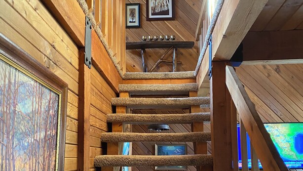 A wooden staircase with a rustic design, framed pictures on the walls, and a television screen displaying a map.