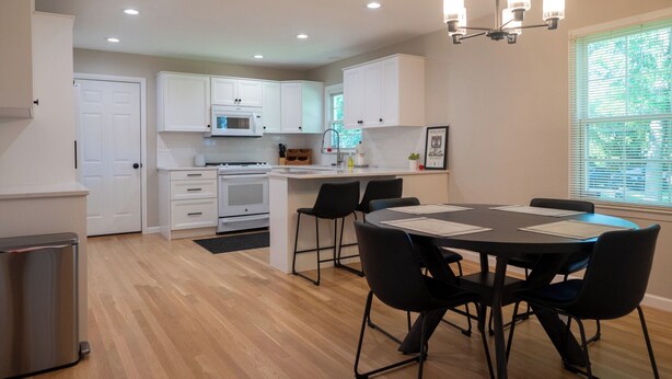 Una cocina moderna con armarios blancos, una isla central y una zona de comedor con una mesa redonda y cuatro sillas.