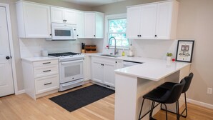 Una cocina moderna con armarios blancos, microondas, estufa, horno y una pequeña isla con taburetes de bar.