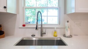 Una cocina moderna con un lavamanos de acero inoxidable, una ventana con vistas a zonas verdes y un dispensador de jabón en la encimera.