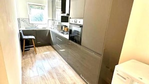 A modern kitchen with a built-in oven, a sink, and a dining area with a chair. - 3 Bedroom Riverview Flat Canary Wharf Free Parking (London)