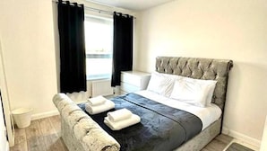 A bedroom with a bed, a bedside table, and a window with curtains. - 3 Bedroom Riverview Flat Canary Wharf Free Parking (London)