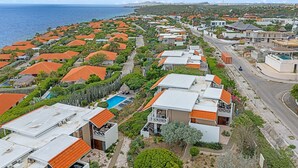 Ein Küstenwohngebiet mit Häusern, die rote Ziegeldächer, einen Swimmingpool und eine Straße zum Meer haben.
