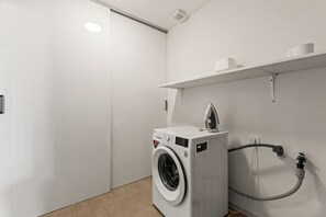 A compact laundry room with a front-loading washing machine, a drying rack, and a hose. - Ocean View Apartment Bayside, 6 guests - Boca Gentil, Jan Thiel area (Jan Thiel)