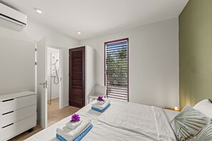 Een moderne slaapkamer met een bed, nachtkastje, dressoir, douche en een raam met zonwering.