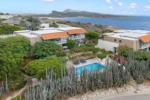 A coastal property with multiple buildings, a swimming pool surrounded by cacti, and a view of the sea. - Ocean View Apartment Bayside, 6 guests - Boca Gentil, Jan Thiel area (Jan Thiel)