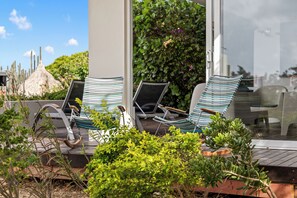 A deck with two lounge chairs, a thatched structure, and lush greenery. - Ocean View Apartment Bayside, 6 guests - Boca Gentil, Jan Thiel area (Jan Thiel)
