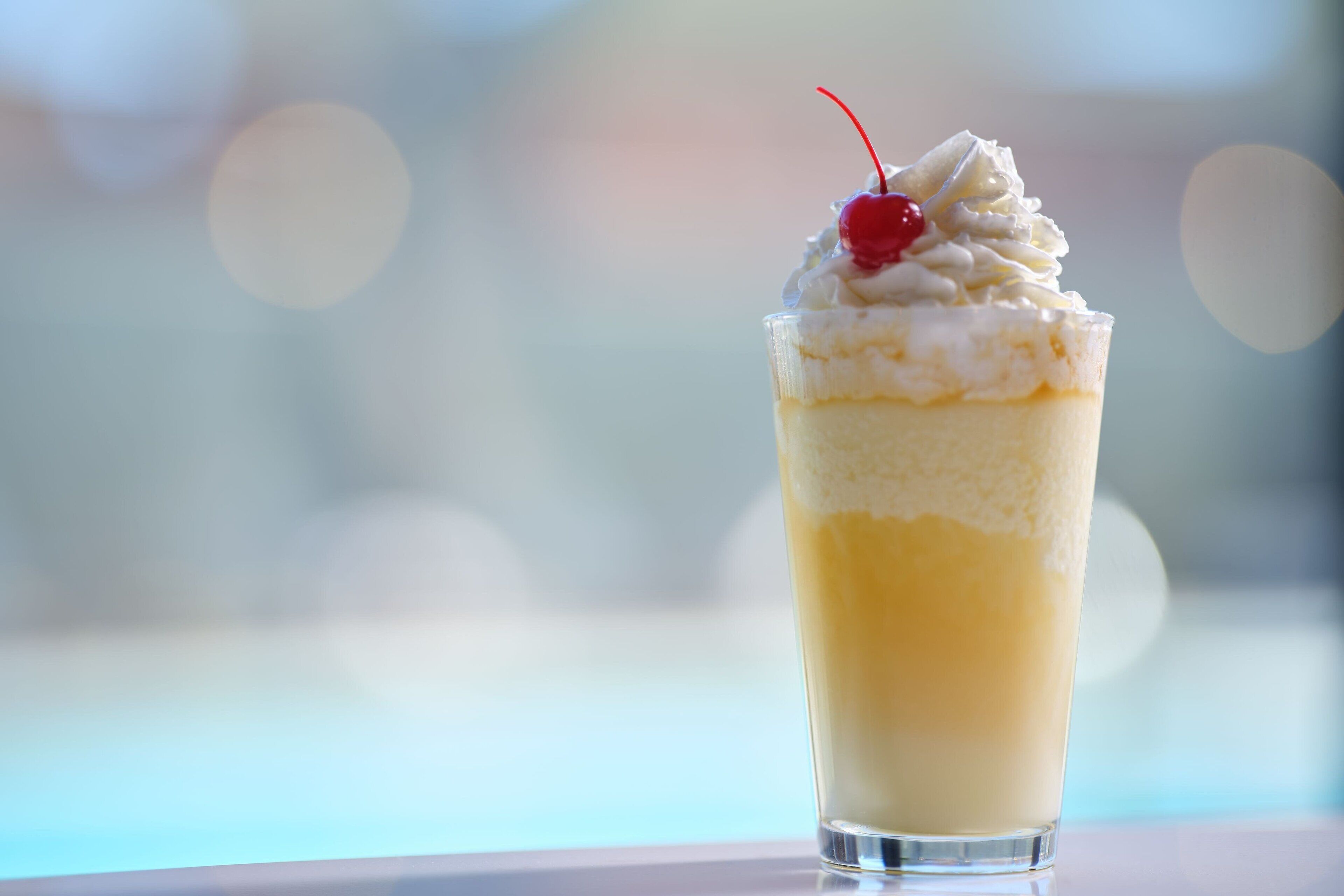 A layered dessert in a clear glass with whipped cream and a cherry on top.