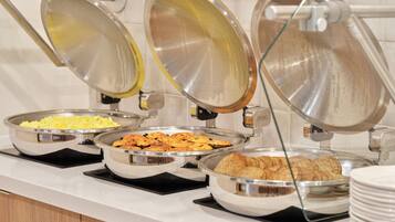 A buffet setup with various food items in metal serving dishes, arranged on a countertop.