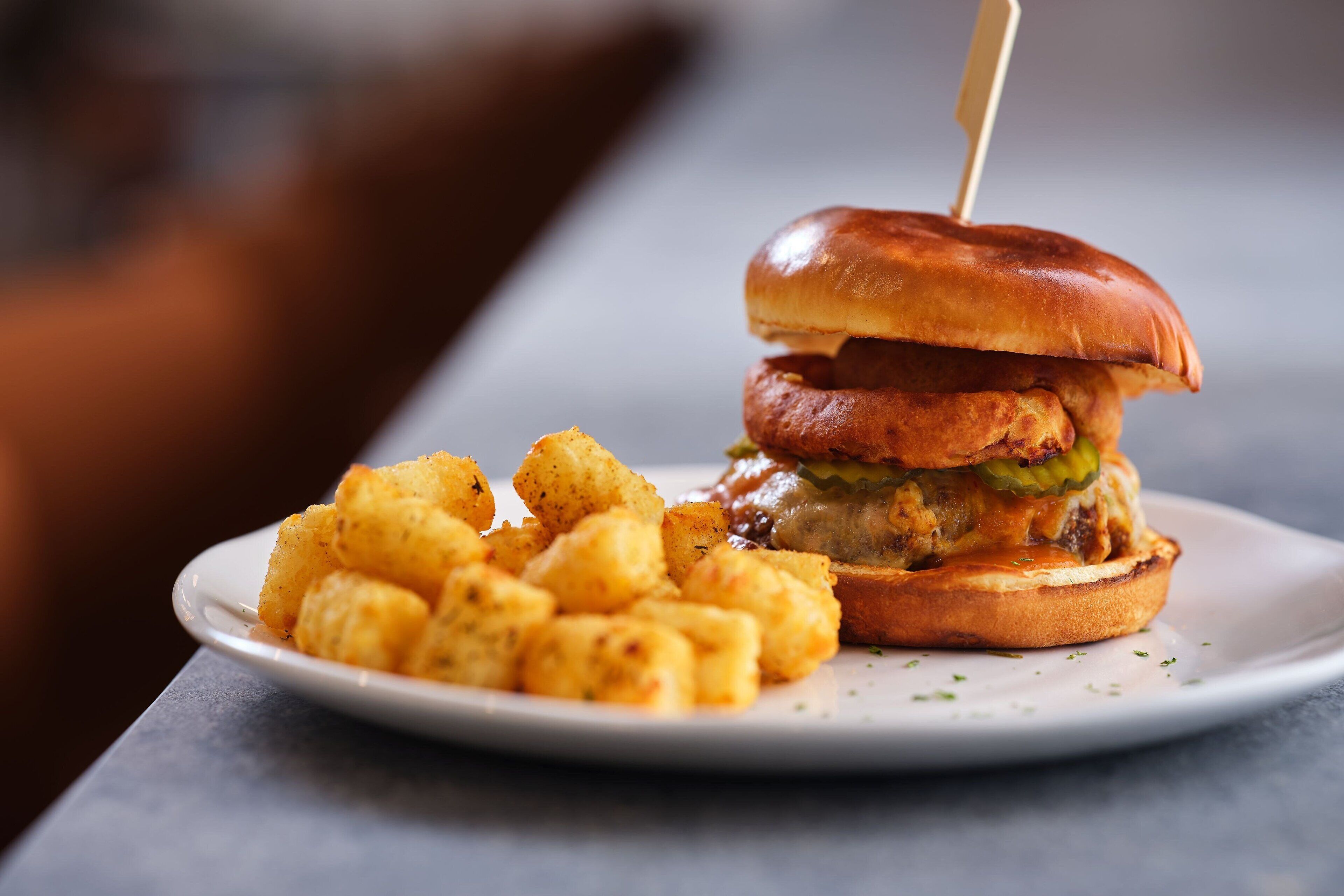 A sandwich with a toothpick, served on a white plate with tater tots.