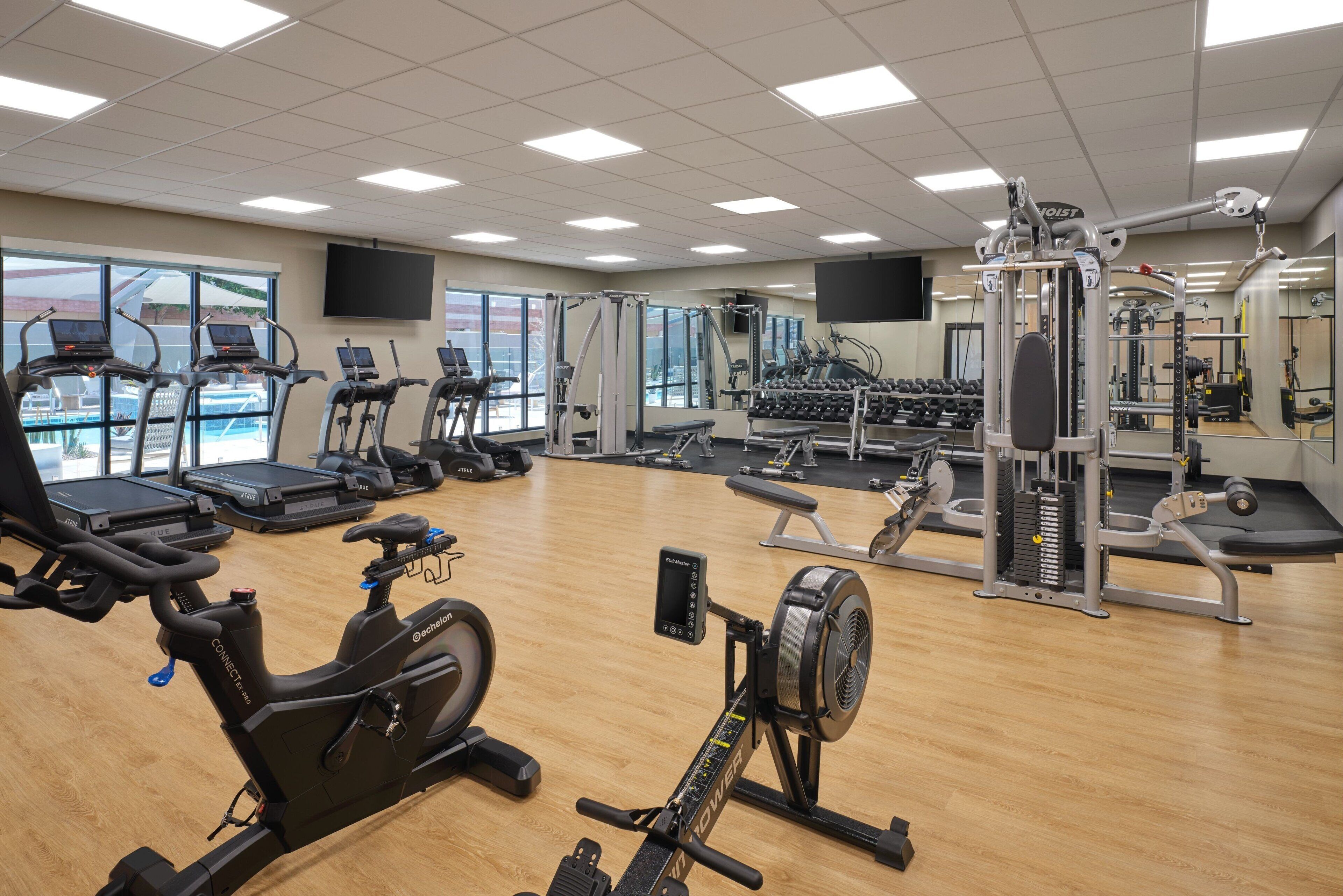 Una palestra con macchinari cardio, aree pesi e specchi.