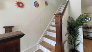 Un escalier avec des marches en bois et une rampe en bois, menant à un palier avec un mur blanc et une fresque décorative représentant le soleil et la lune.